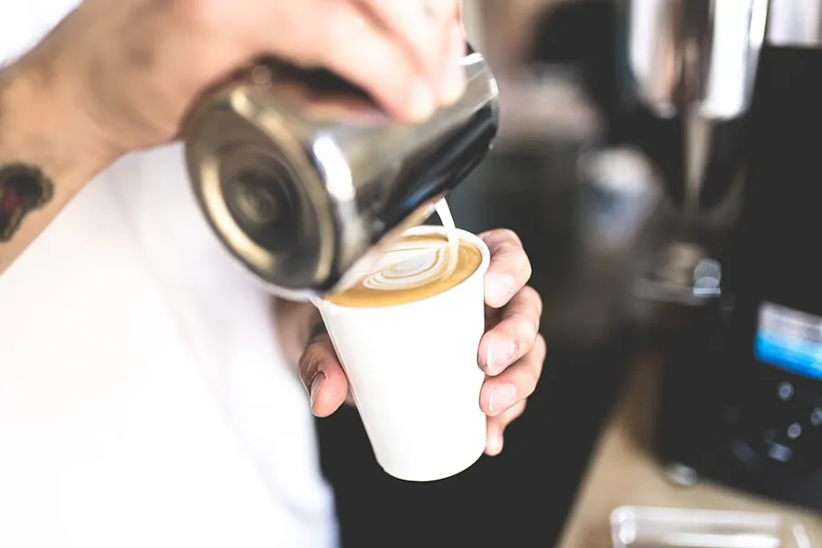 Barista gießt Milch in eine Tasse Kaffee